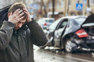 AI generated A man holds his head with his hands against the background of a broken car, a car accident on a city street